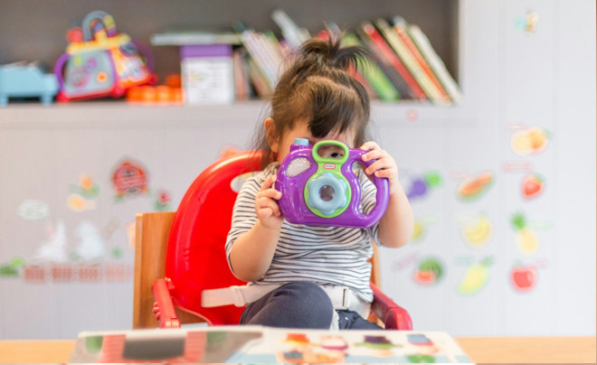 Em bé ngồi giữa rất nhiều đồ chơi giáo dục và sách, minh họa chi phí đồ chơi phát triển trí tuệ