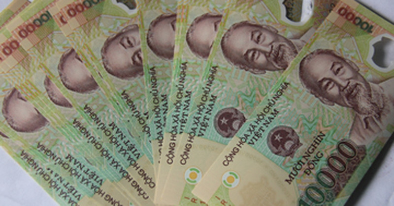 Bàn tay đang cầm tờ tiền 10.000 VNĐ, biểu thị giá trị của **1 xị** trong cách gọi thông thường của người Việt Nam